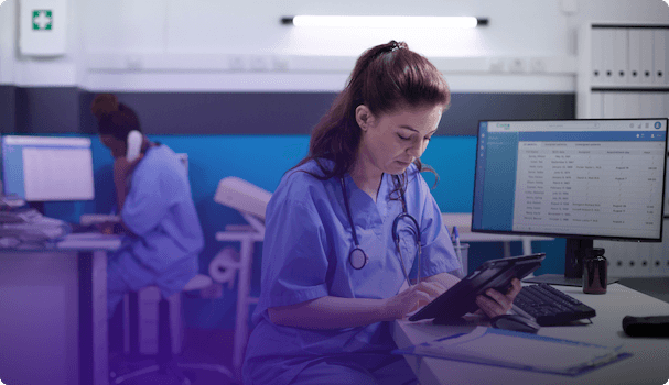 Image d'une infirmière consultant un appareil numérique dans une salle d'hôpital équipée de divers moniteurs et ordinateurs, reflétant l'activité quotidienne dans le secteur médical.